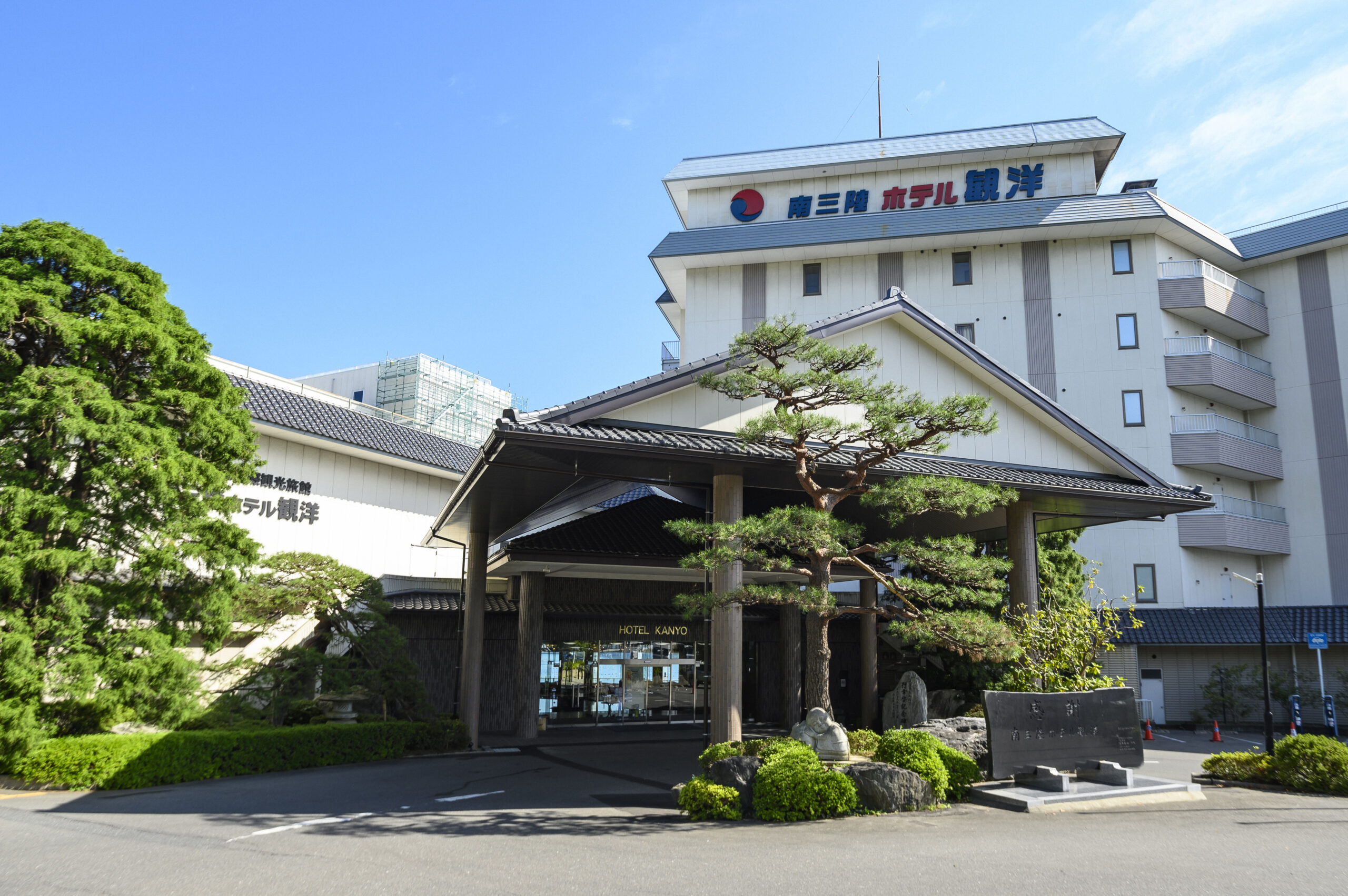 Hotel entrance with a traditional roof and green landscaping; sign reads HOTEL KANYO in English.