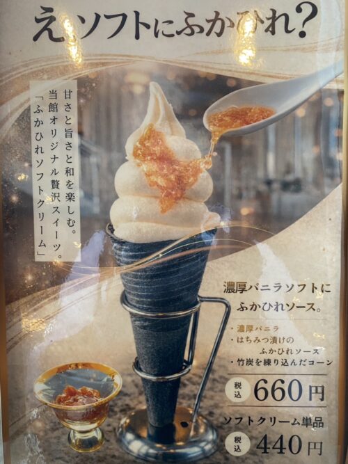 Vanilla soft-serve ice cream swirled high, with orange sauce being poured from a spoon onto the top, in a metal holder (advertising poster).