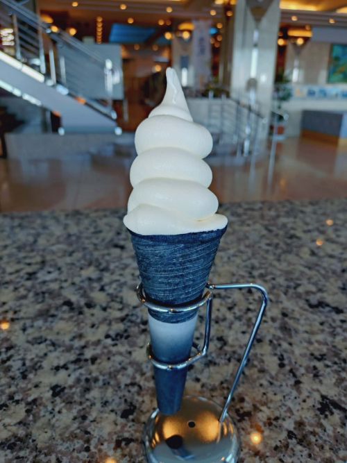 Soft-serve vanilla ice cream in a dark blue cone on a metal stand, indoors at a modern cafe.