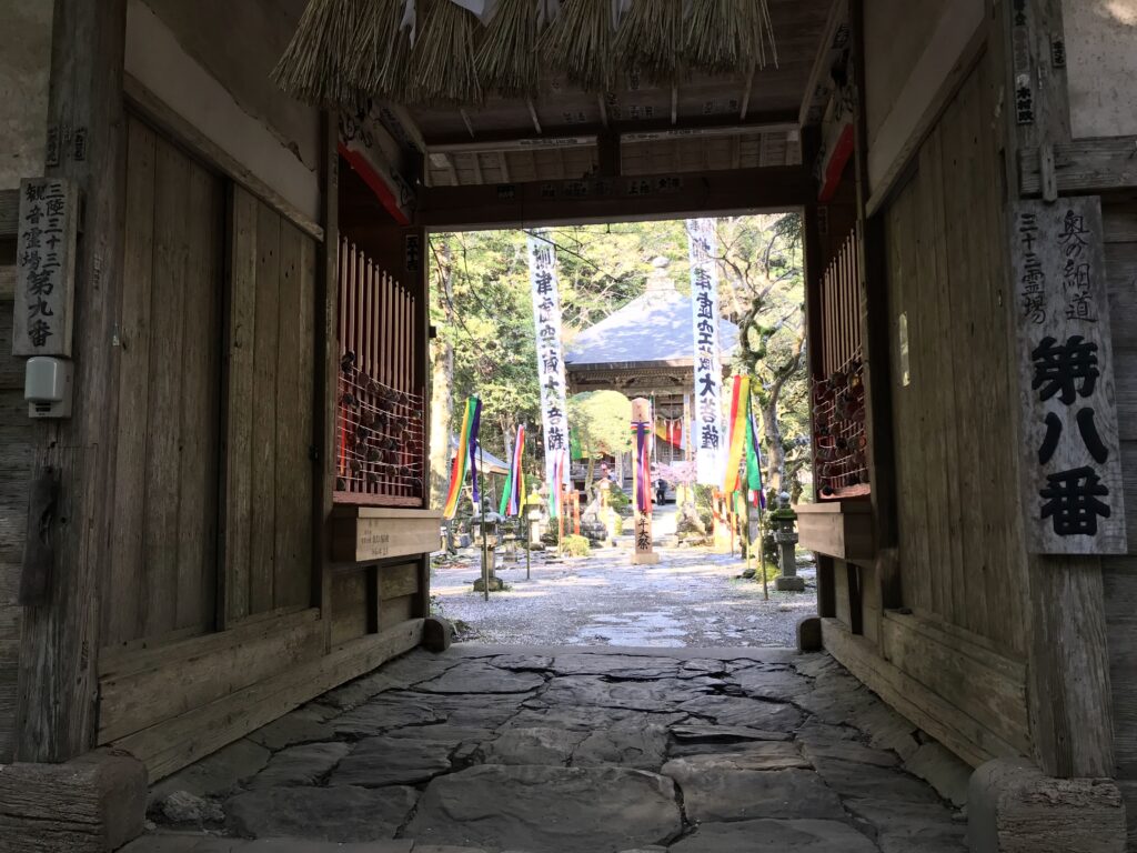 Wooden temple gate opening to a stone path with colorful banners and a shrine in the background