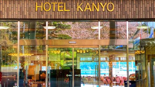 Front entrance of Hotel Kanyo with glass doors, warm interior lighting, and wooden facade above.