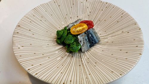 Gourmet dish: greens, a yellow citrus half, and two pieces of fish on a ridged ceramic plate.