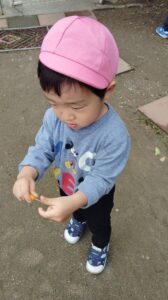 Small child wearing a pink cap and blue Mickey Mouse shirt outdoors, holding a tiny orange object.