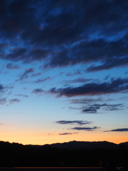 Silhouette of hills along the horizon at dusk with an orange-to-blue gradient sky and dark clouds.