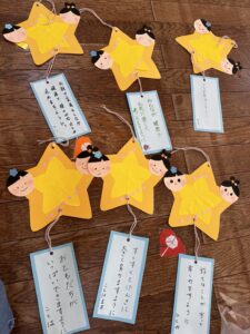 Yellow star-shaped decorations with smiling paper faces and hanging blue tags on a wooden floor surface.