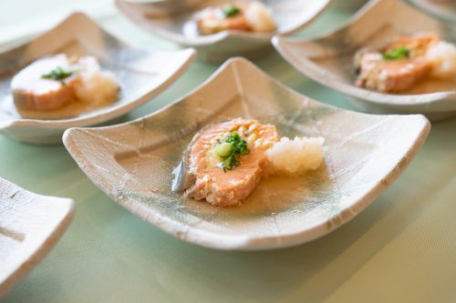 Leaf-shaped ceramic plate with a salmon bite, garnished with greens and grated radish on a pale table.