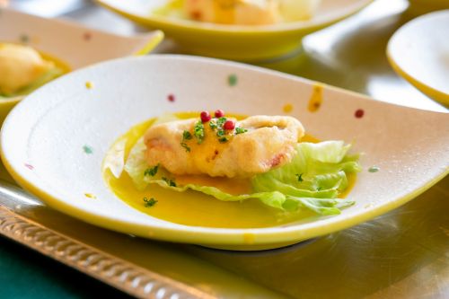 Pan-seared fish fillet on a lettuce leaf, drizzled with yellow sauce, garnished with herbs and pink peppercorns on a yellow-rimmed plate.