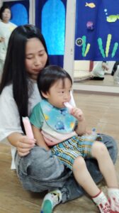 Mother holding a young child on her lap while the child eats a pink popsicle indoors.