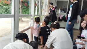 People, including children, kneel and sit inside a glass-walled vehicle with colorful decorations on the windows, looking outside or taking photos.