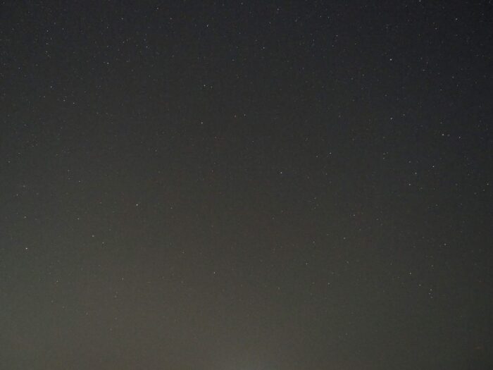 Wide view of a star-filled night sky above a dark horizon or landscape.